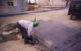 Un hombre que lleva un casco verde está trabajando en una acera.
