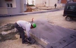 Un hombre que lleva un casco verde está trabajando al costado de una carretera.