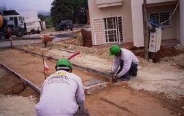 Dos obreros de la construcción están trabajando en una acera frente a una casa.