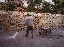 Un hombre está usando una hidrolavadora para limpiar una pared de piedra.