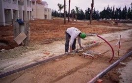 Un trabajador de la construcción está trabajando en una acera en un campo de tierra.