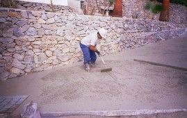 Un hombre está usando una escoba para esparcir cemento en el suelo.