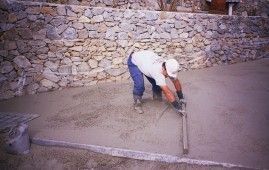 Un hombre está colocando hormigón en el suelo frente a un muro de piedra.