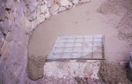 Una tapa de alcantarilla está colocada en el suelo junto a un muro de piedra.