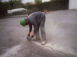 Un hombre está usando una amoladora en un camino de entrada de hormigón.