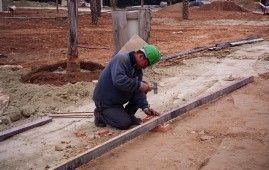 Un trabajador de la construcción está arrodillado en el suelo sosteniendo un martillo.