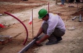 Un trabajador de la construcción que lleva un casco verde está arrodillado en el suelo.