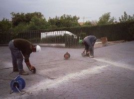 Dos hombres están trabajando en una superficie de concreto en un estacionamiento.