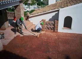 Dos hombres están pintando un piso de ladrillo con una escoba.