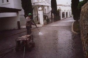 Un hombre está limpiando la acera con una hidrolavadora.