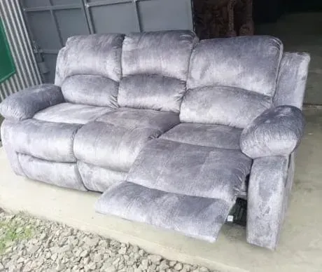 A grey recliner couch is sitting on a concrete floor.