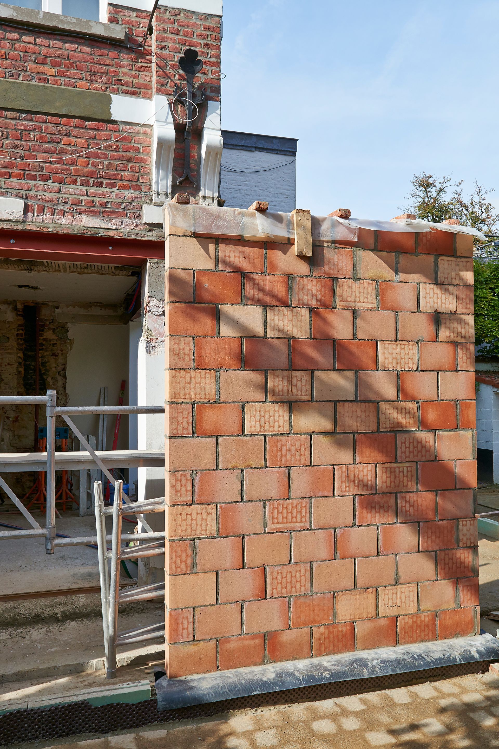 Mur de briques en construction à côté de la façade d'un bâtiment.