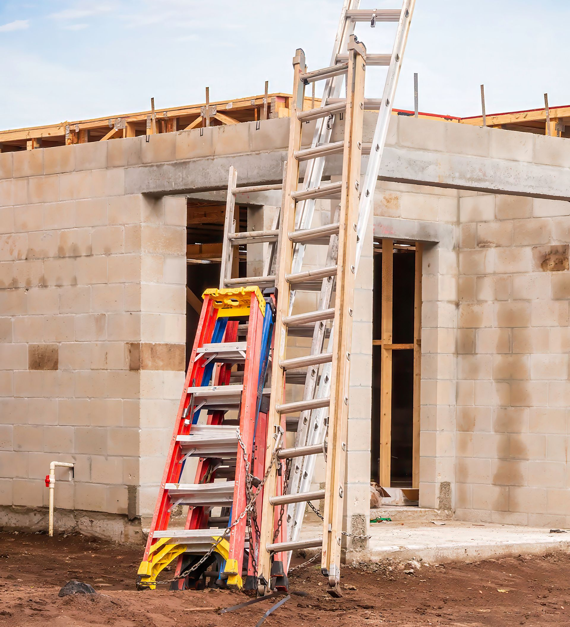Trois échelles appuyées contre un bâtiment en parpaings en construction.