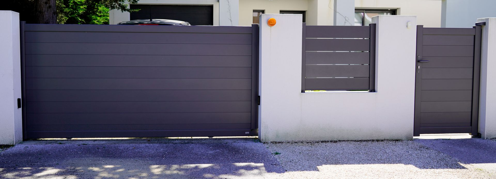 Un portail d'allée et un portail d'entrée, encastrés dans des murs en béton blanc.