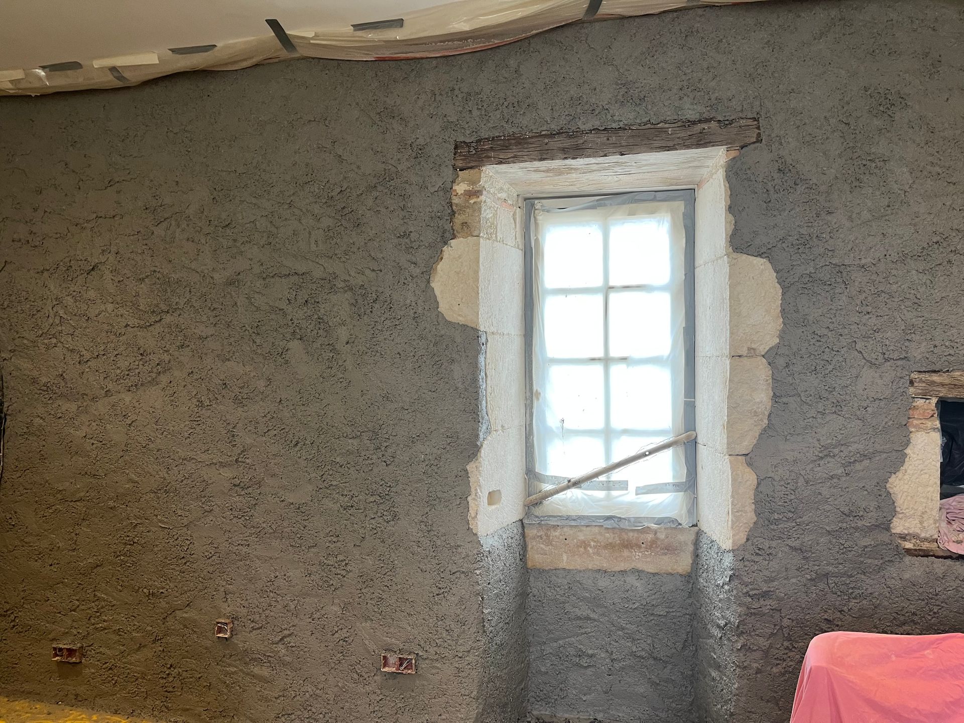 Mur intérieur avec fenêtre, finition en plâtre gris texturé.