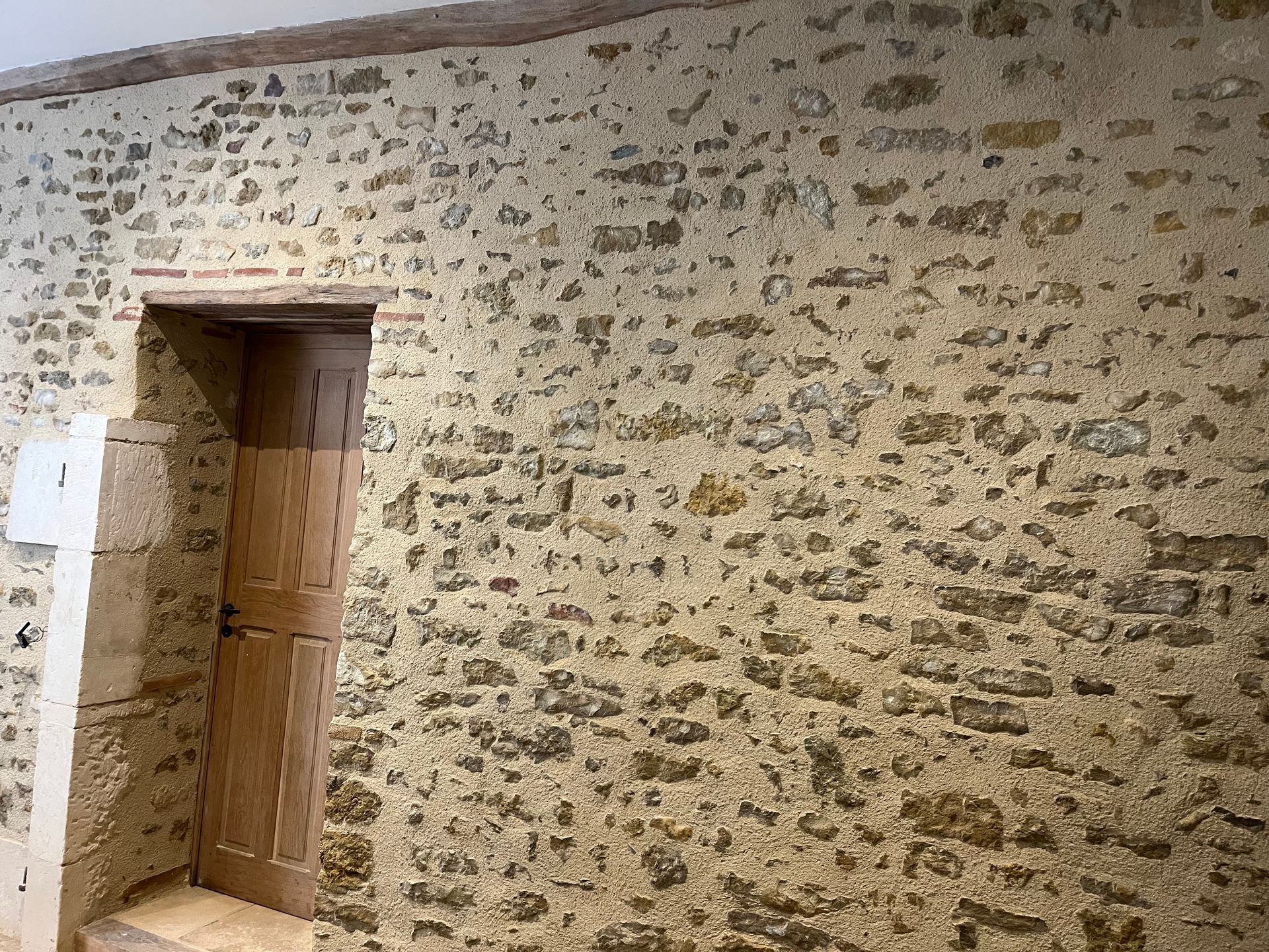 Mur en pierre avec porte en bois, probablement l'intérieur d'un ancien bâtiment.