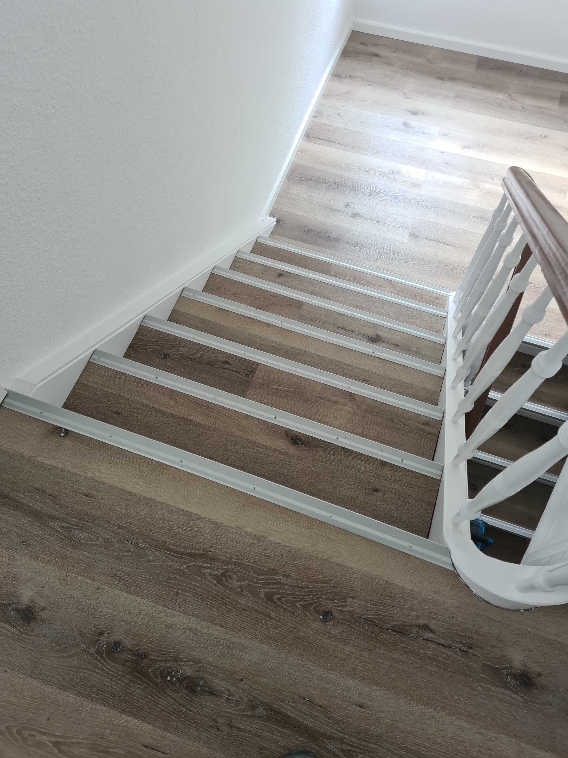 Treppe mit weißen Setzstufenprofilen und hellem Holzfußboden, aufgenommen von oben.