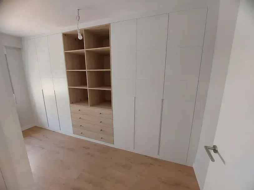 Un dormitorio con armarios blancos y estantes y cajones de madera.