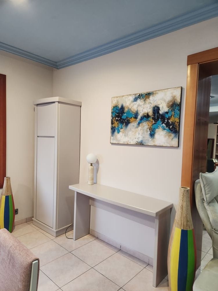 Una entrada moderna con un armario alto, una mesa consola, arte abstracto en la pared y dos grandes jarrones de suelo de colores.