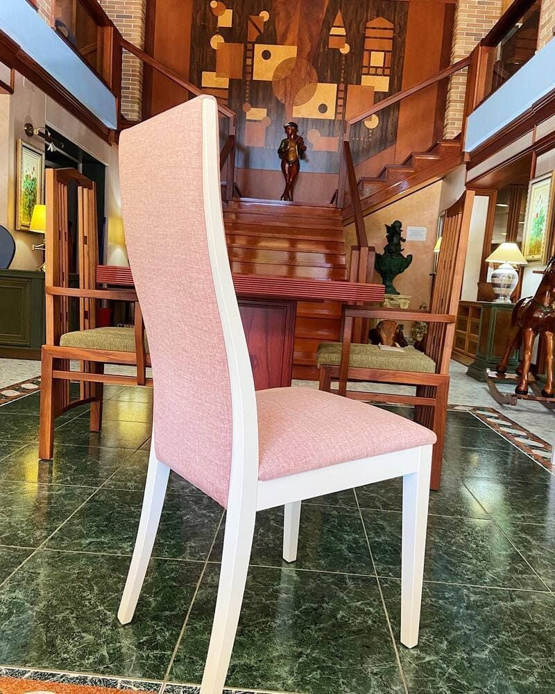 Una silla de comedor moderna con respaldo alto tapizado en rosa y patas de madera blanca, ubicada en un interior elegante de varios niveles.