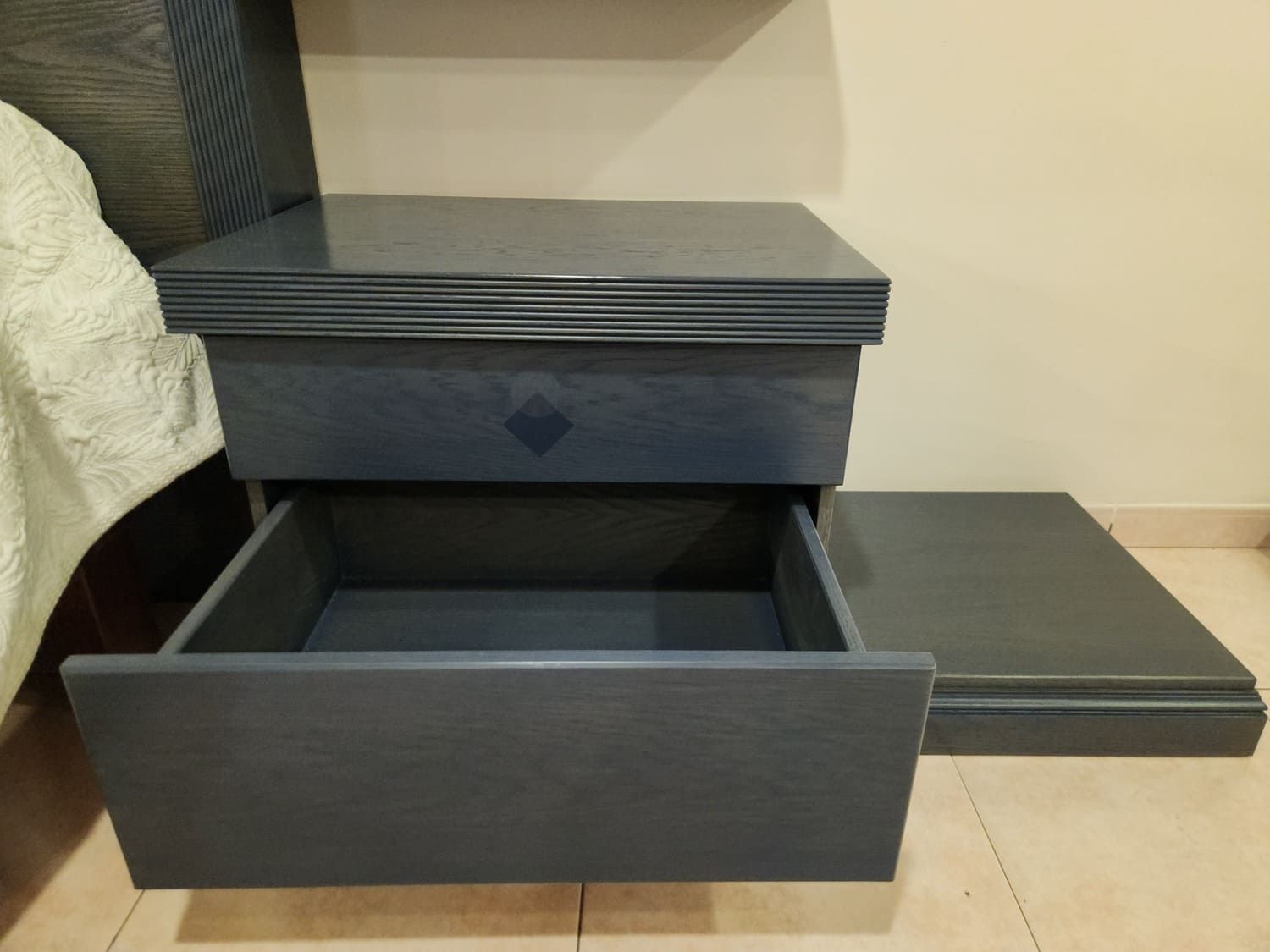 Mesita de noche azul con cajón abierto y mesa auxiliar independiente.