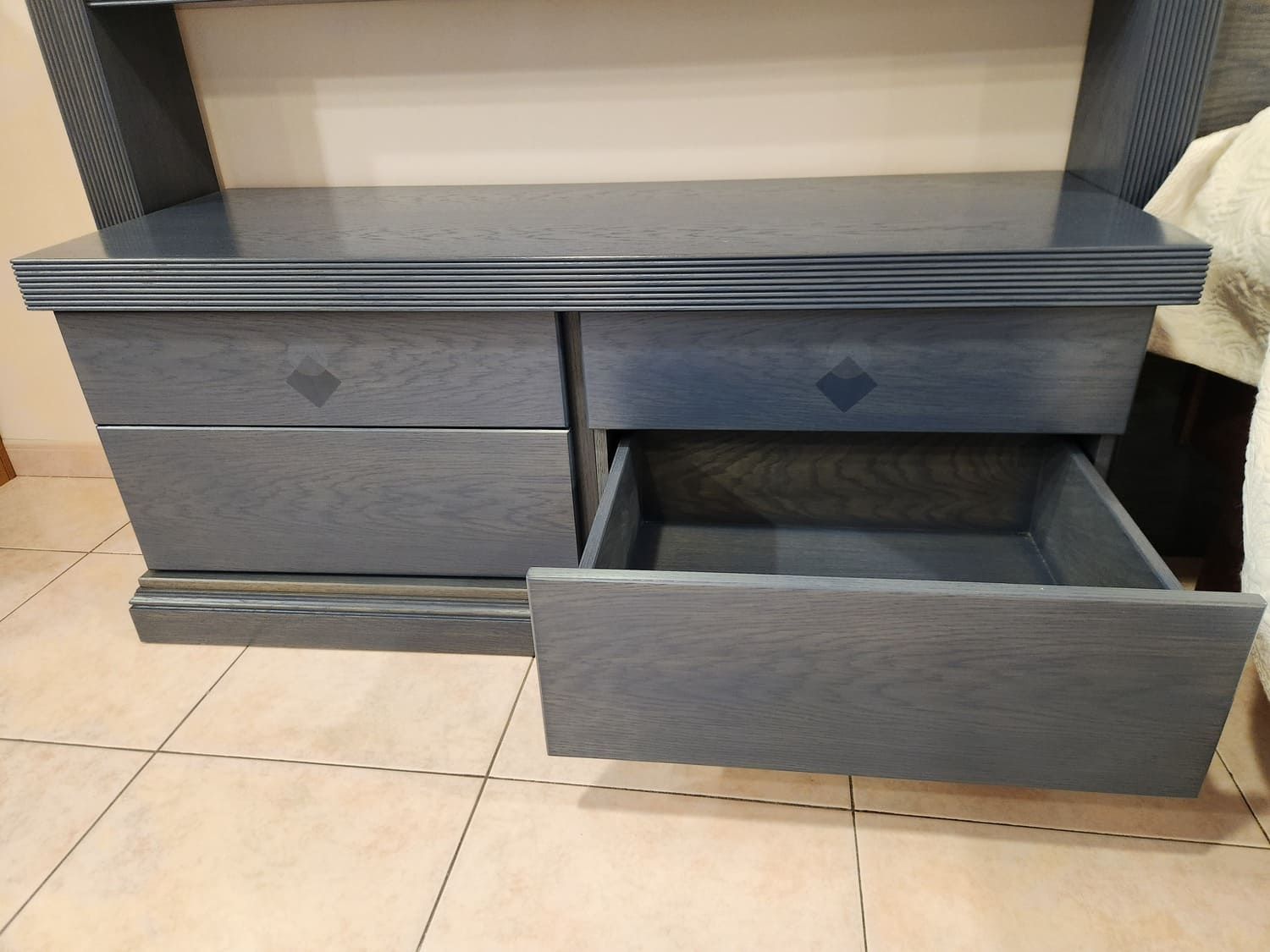 Cómoda azul con un cajón abierto, debajo de un estante, contra una pared.