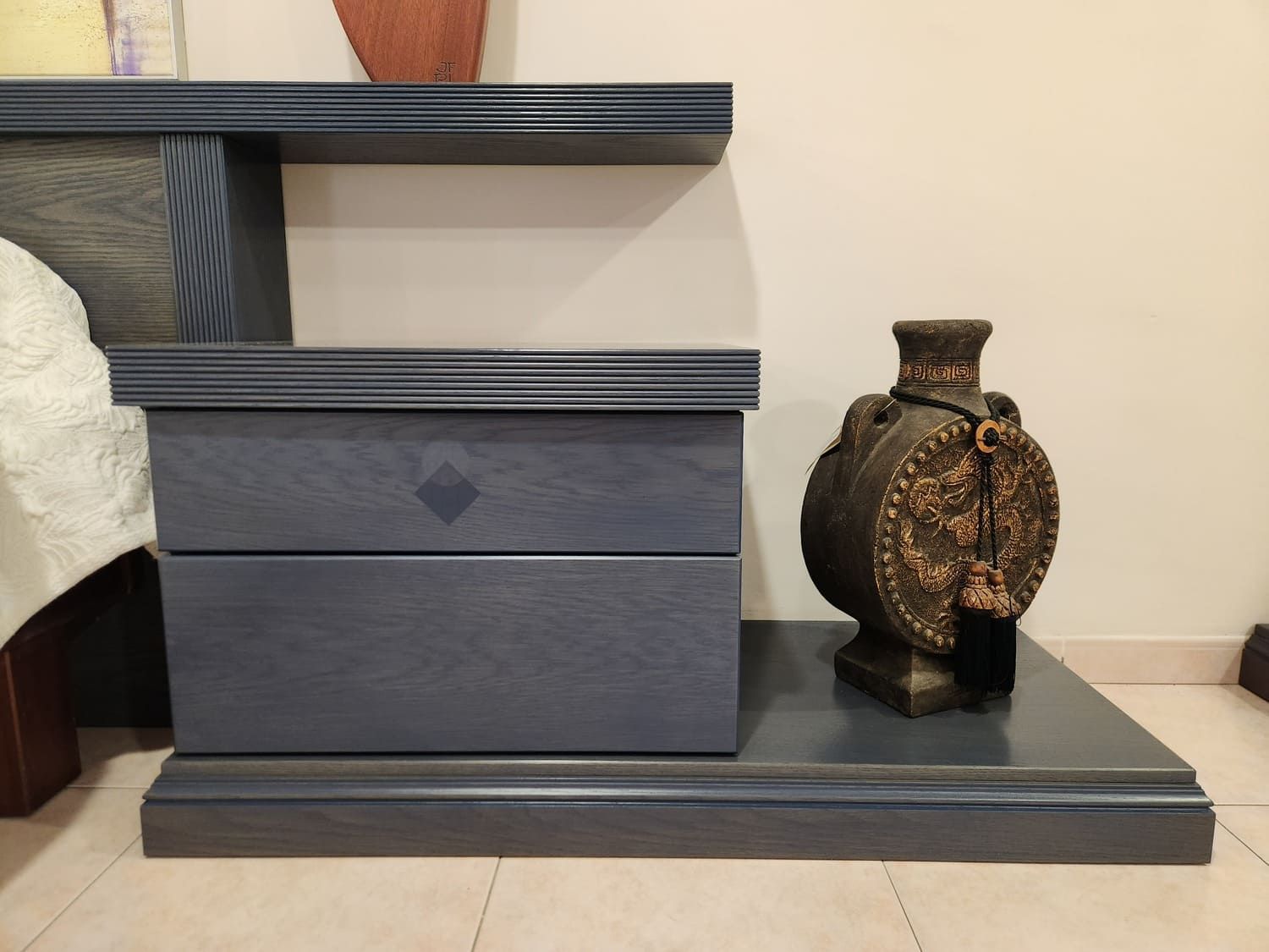 Mesita de noche gris con dos cajones, jarrón decorativo y estante.