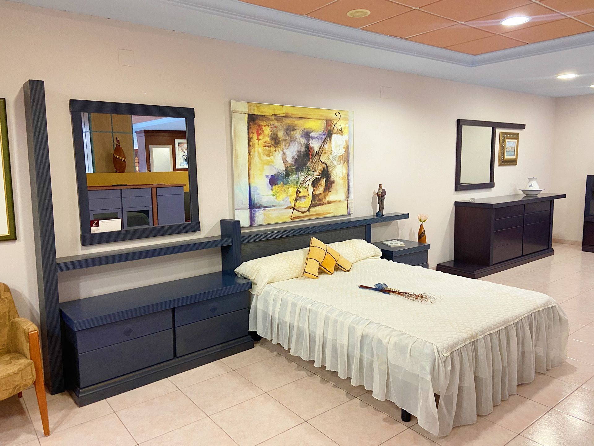 Conjunto de muebles de dormitorio: cama con ropa de cama blanca, mesita de noche, cómoda, espejos y cuadro abstracto.