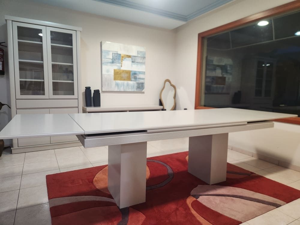 Una mesa de comedor blanca con una extensión lateral se encuentra sobre una alfombra estampada en rojo y naranja en un comedor muy iluminado.