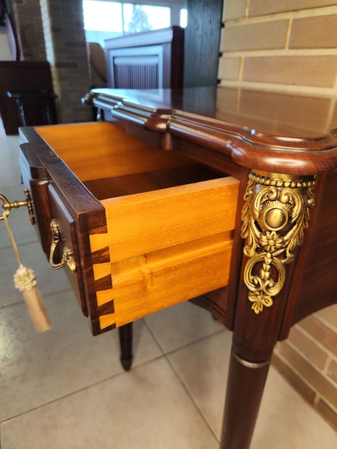 Mesa antigua de madera con cajón abierto, con uniones de cola de milano. Detalles y herrajes dorados.