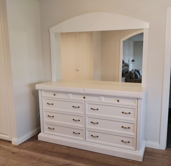 Una cómoda blanca con cajones y un espejo en un dormitorio.