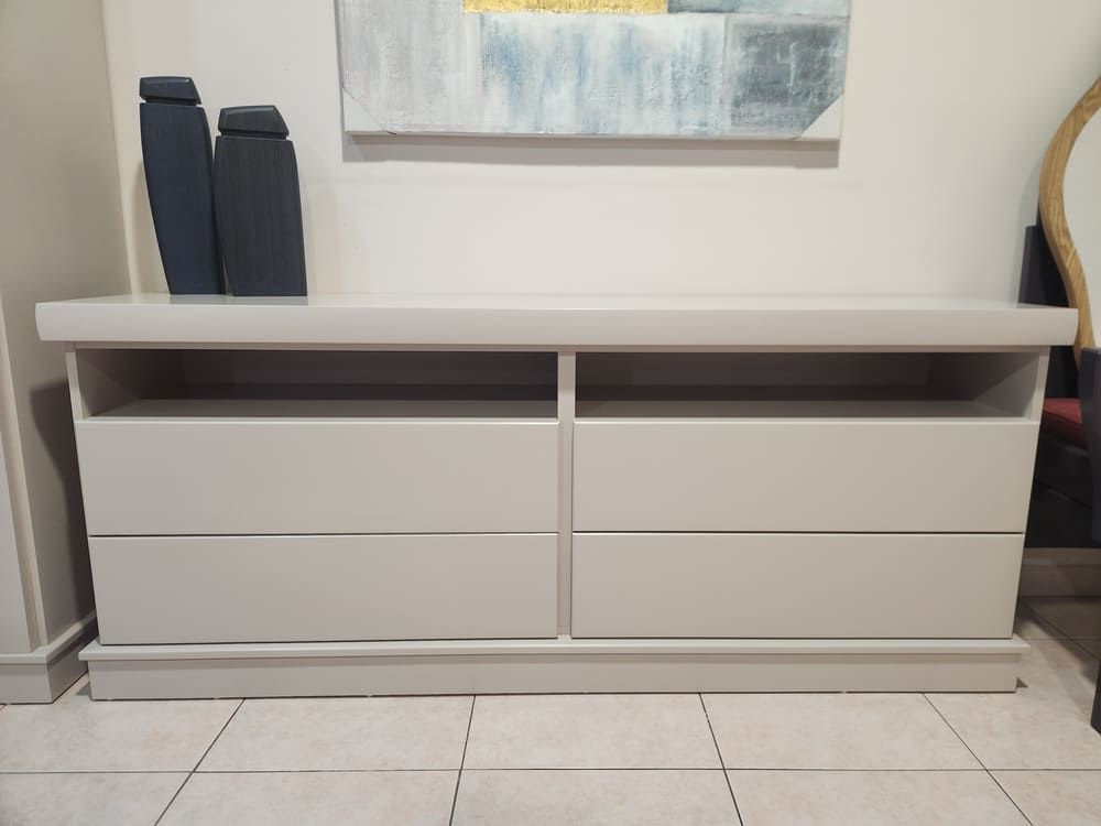 Un aparador de madera gris claro con seis cajones y un estante abierto en la parte superior, colocado contra una pared blanca.