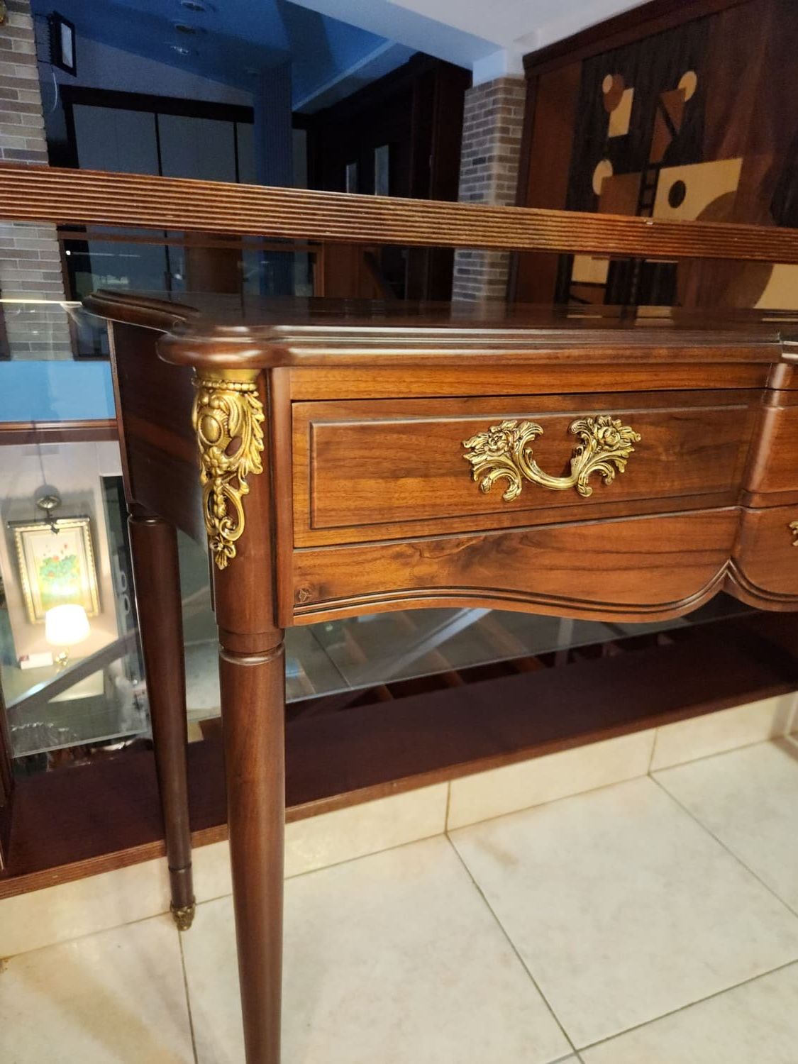 Escritorio de madera con tiradores de cajones ornamentados y detalles en las esquinas; ubicado en un edificio con un balcón que da a un nivel inferior.