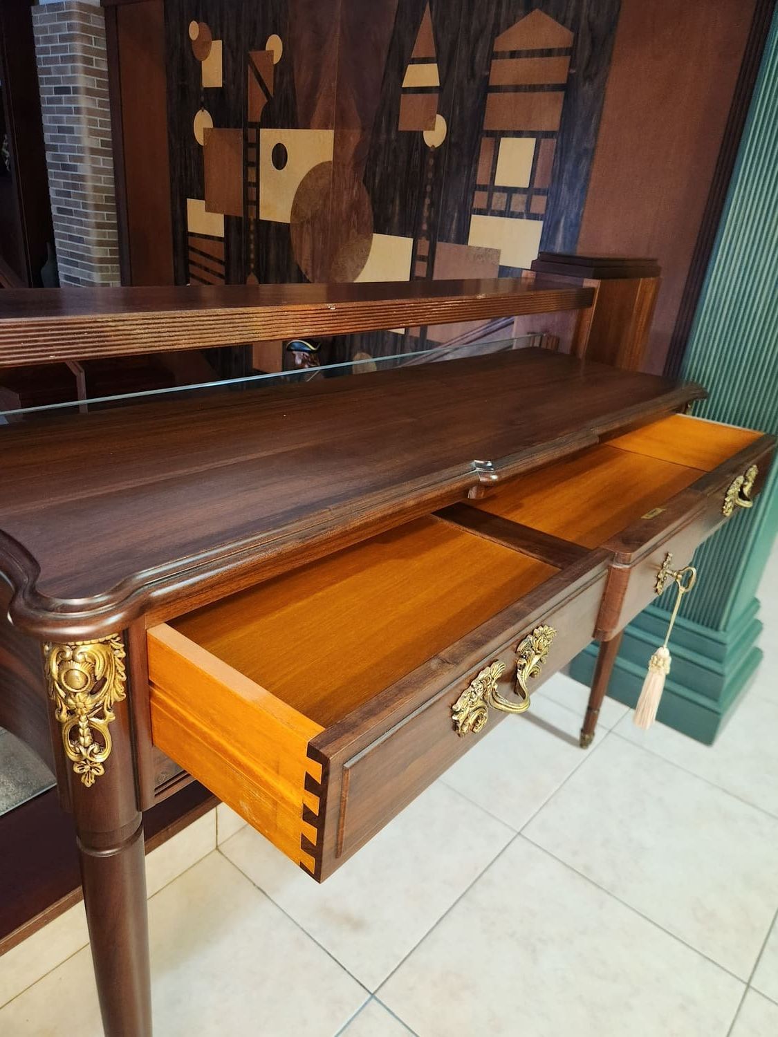 Consola de madera oscura con cajones abiertos, herrajes dorados y incrustaciones de madera en el fondo.
