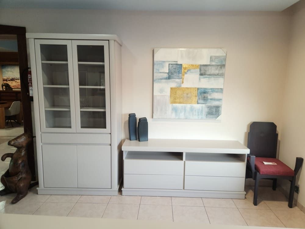 En una habitación hay un armario de color claro, una mesa consola con dos jarrones, un cuadro decorativo en la pared y una silla oscura.