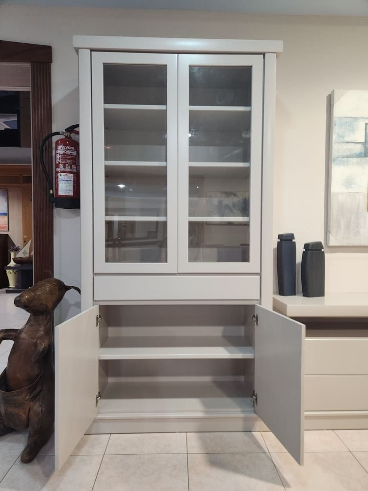 Un armario alto de madera gris claro con puertas de cristal en la parte superior, un estante abierto y puertas en la parte inferior, situado en una habitación.
