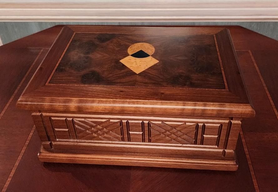 Caja de madera con diseño incrustado sobre una mesa de madera oscura.