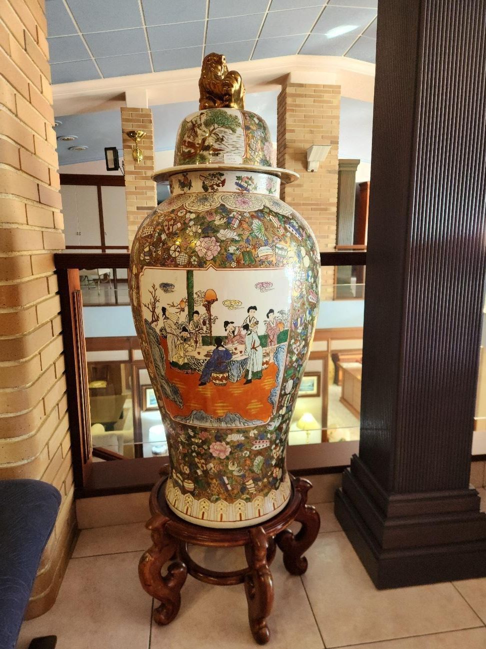 Gran jarrón de porcelana ornamentado con tapa sobre soporte de madera. Coloridos diseños florales y figurativos.