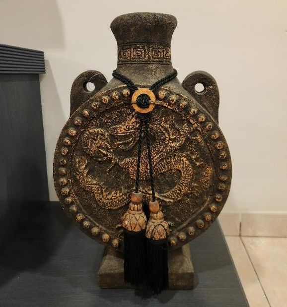 Jarrón de piedra con relieve de dragón y borla decorativa.