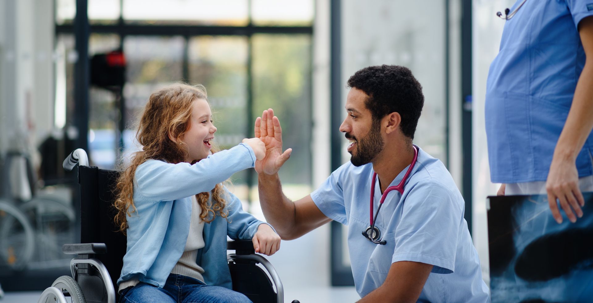 Un infirmier fait un check à une jeune fille en fauteuil roulant souriante