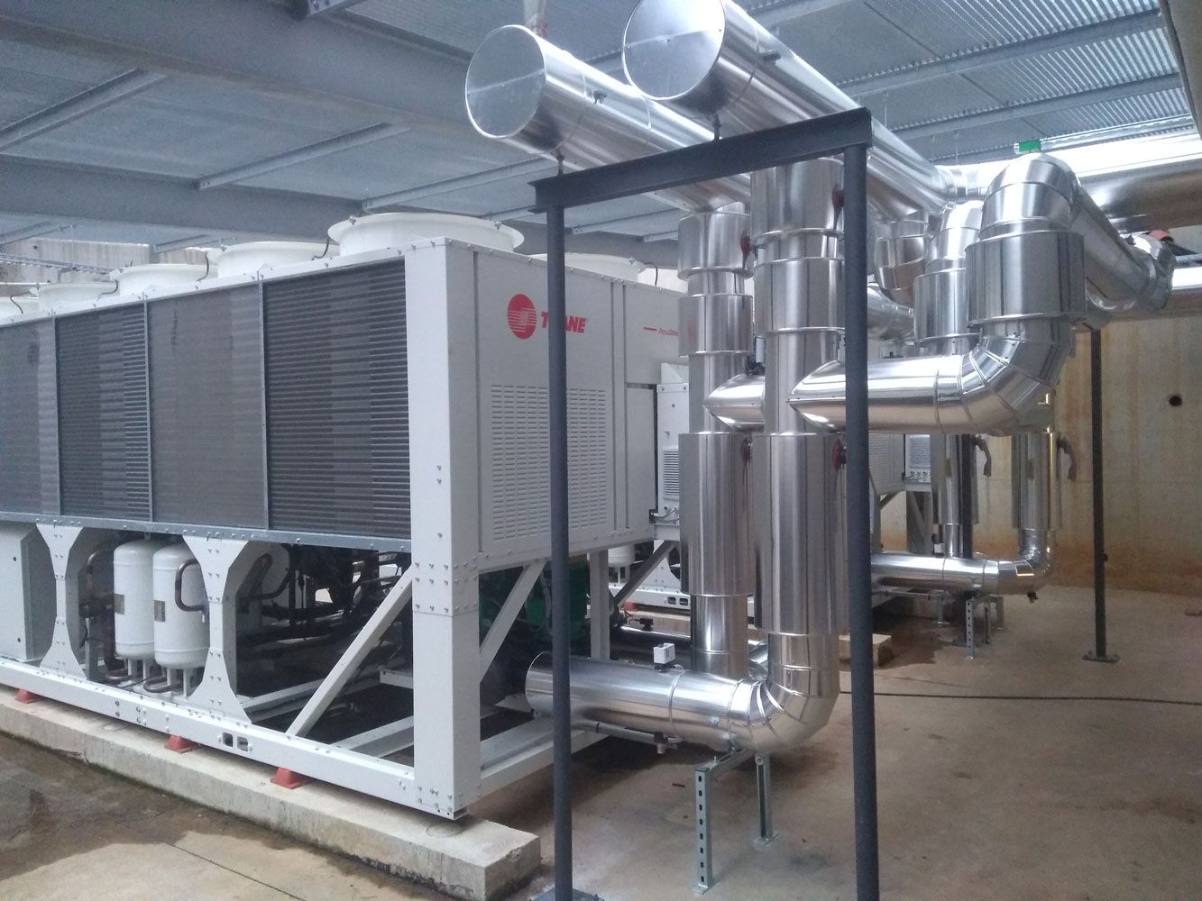 Groupes frigorifiques et tuyauterie isolée dans une salle des machines industrielle.