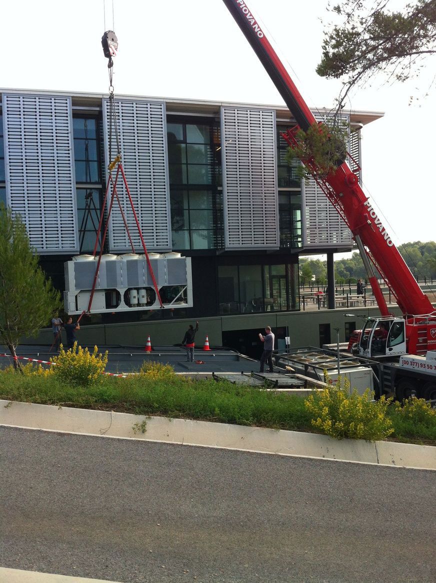 Grue soulevant une unité de climatisation pour l'installer sur un bâtiment moderne.