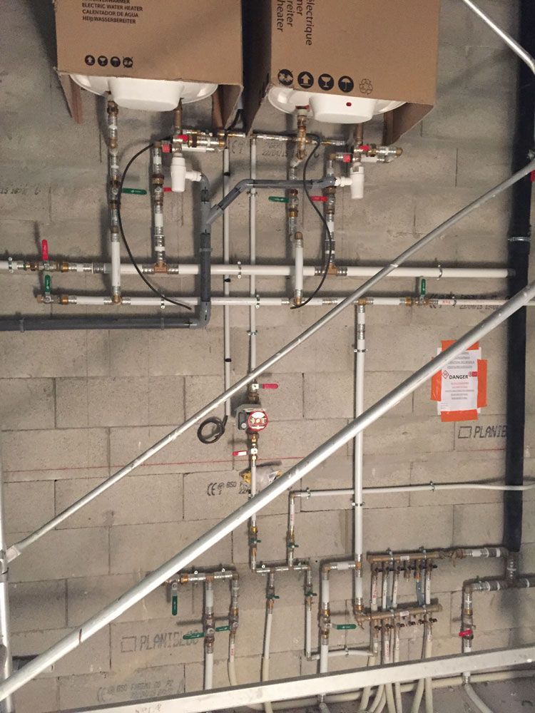 Système de plomberie comprenant plusieurs tuyaux, vannes et chauffe-eau montés sur un mur en béton dans un bâtiment en construction.