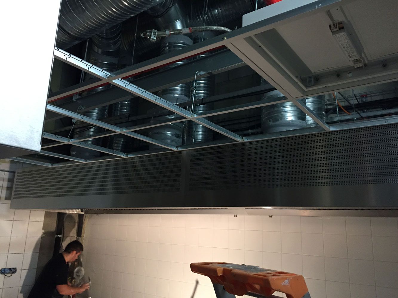 Un homme travaille sur un plafond à ossature métallique, comportant des conduits et un système de ventilation.