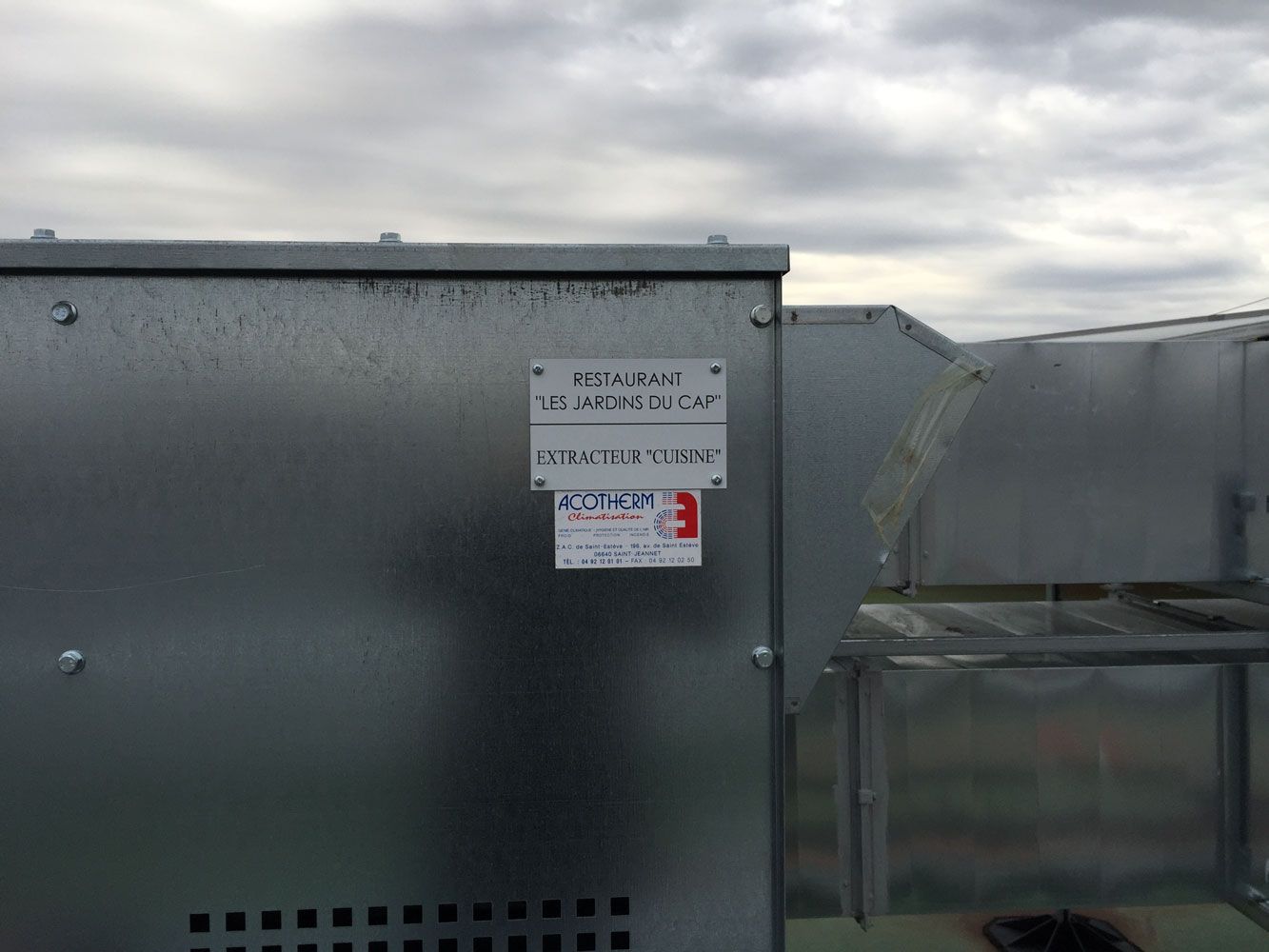 Boîtier métallique et conduits d'aération sur le toit sous un ciel nuageux, avec étiquettes d'identification apposées.
