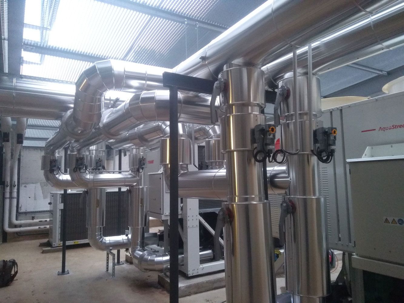 Tuyauterie et machines en milieu industriel, avec tuyauterie argentée isolée et boîtiers de commande.