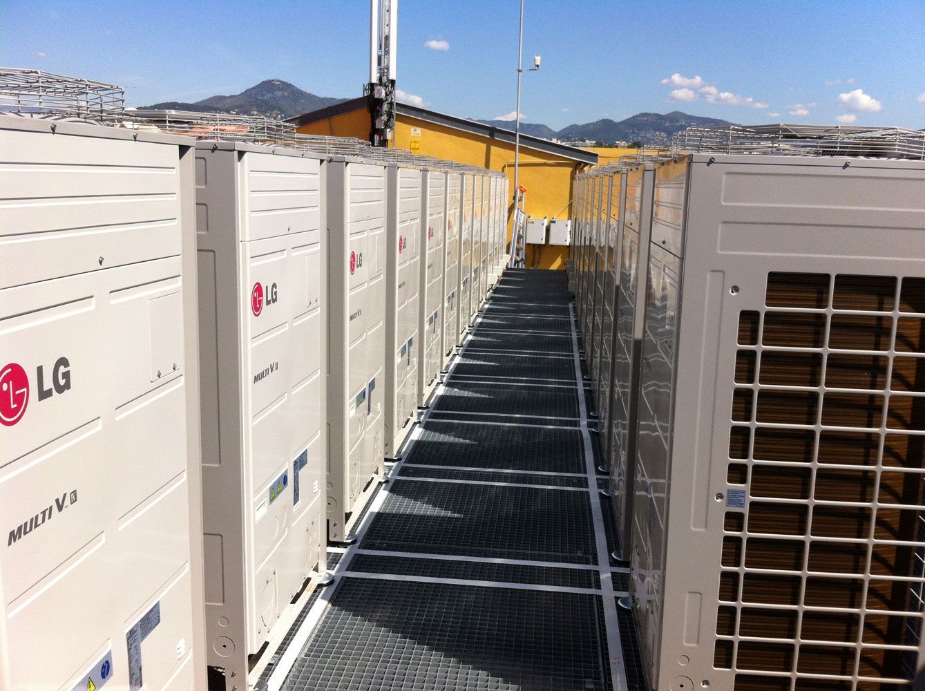 Rangée d'unités de climatisation LG sur un toit-terrasse avec une passerelle métallique.