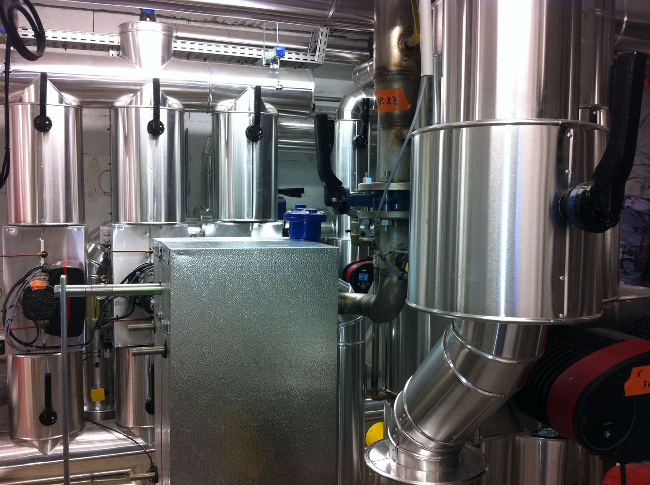 Tuyaux et équipements industriels à surfaces argentées isolées dans un local technique.