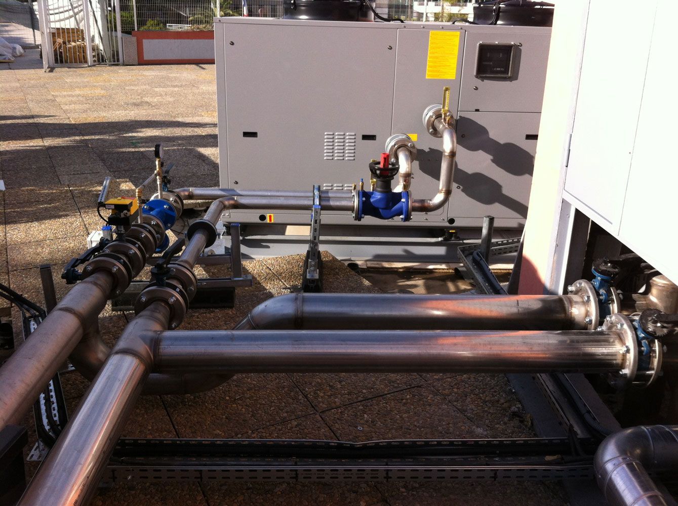 Équipement industriel extérieur avec tuyauterie en cuivre, vannes et boîtier métallique gris.