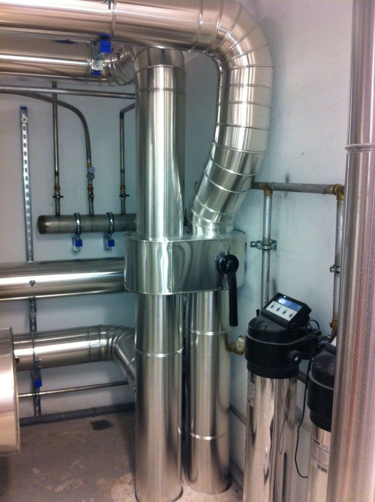 Dans un local technique, on trouve des tuyaux et des équipements isolés. Des tuyaux métalliques argentés relient différents appareils ; un panneau numérique est visible.